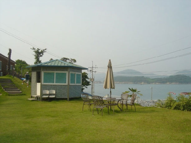 만지도 민박집 마당의 넓은 잔디밭 위에 통나무집과 멀리 바다가 보이는 사진